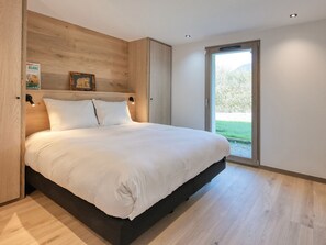 Quarto moderno com uma cama grande, cabeceira de madeira e vista para uma paisagem verde através de uma porta deslizante.