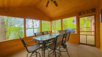 A wooden cabin with a dining table and chairs, large windows, and an American flag.