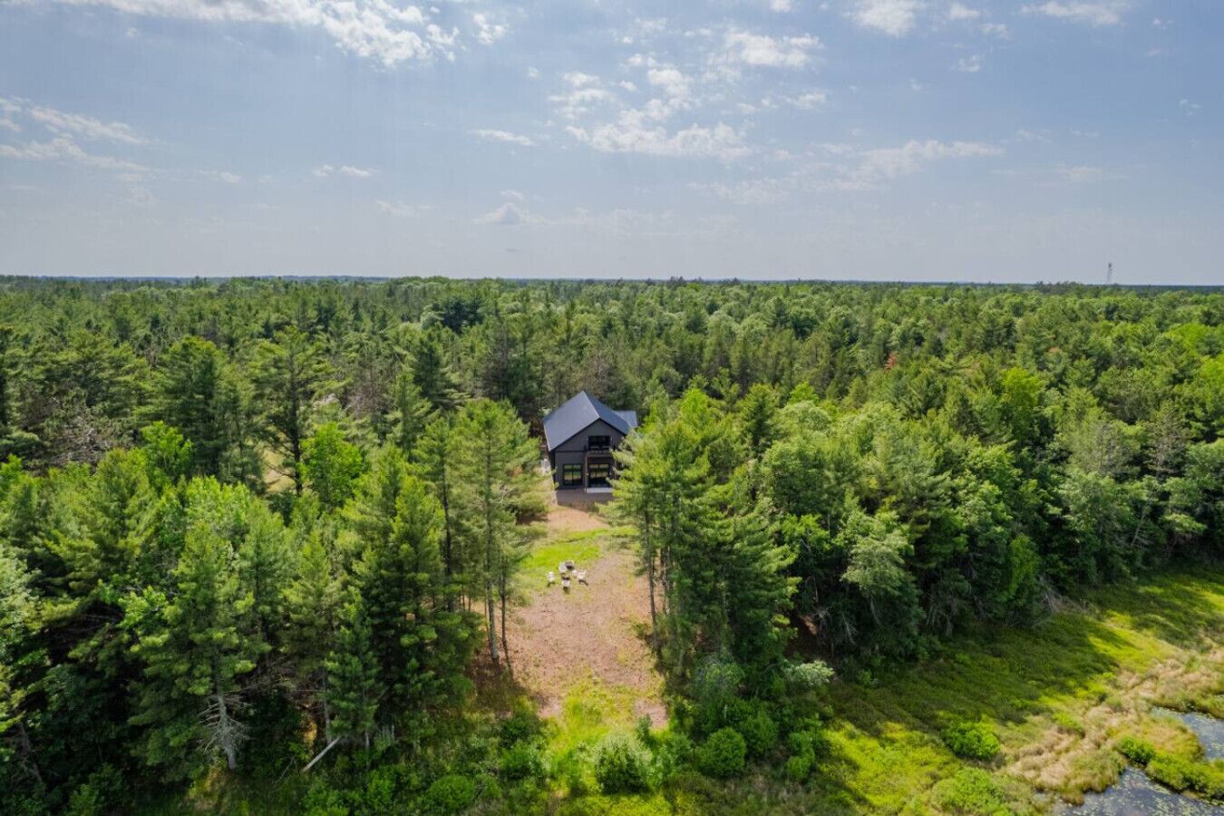 Syvällä metsän keskellä sijaitseva eristäytynyt mökki, jonka yläpuolella on kirkas taivas.