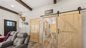 Een kamer met een grote houten deur, een opgehangen hertenkop en een grijze leren bank.