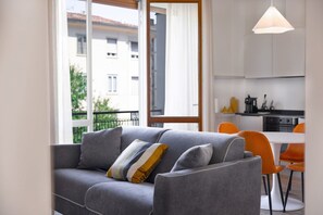 Una sala de estar moderna con un sofá gris, un cojín amarillo y un comedor con sillas naranjas.