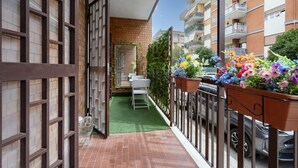 Un balcone con prato artificiale verde, un tavolo e sedie bianche e vasi di fiori.