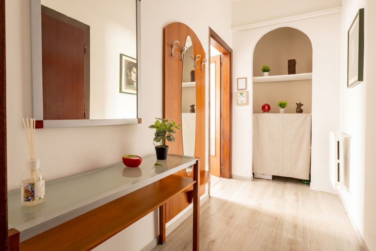 Un corridoio con una porta in legno, uno specchio, una pianta e un portasciugamani bianco.