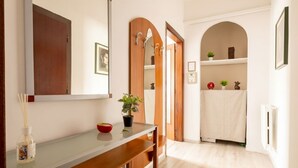 Un corridoio con una porta in legno, uno specchio, una pianta e un portasciugamani bianco.