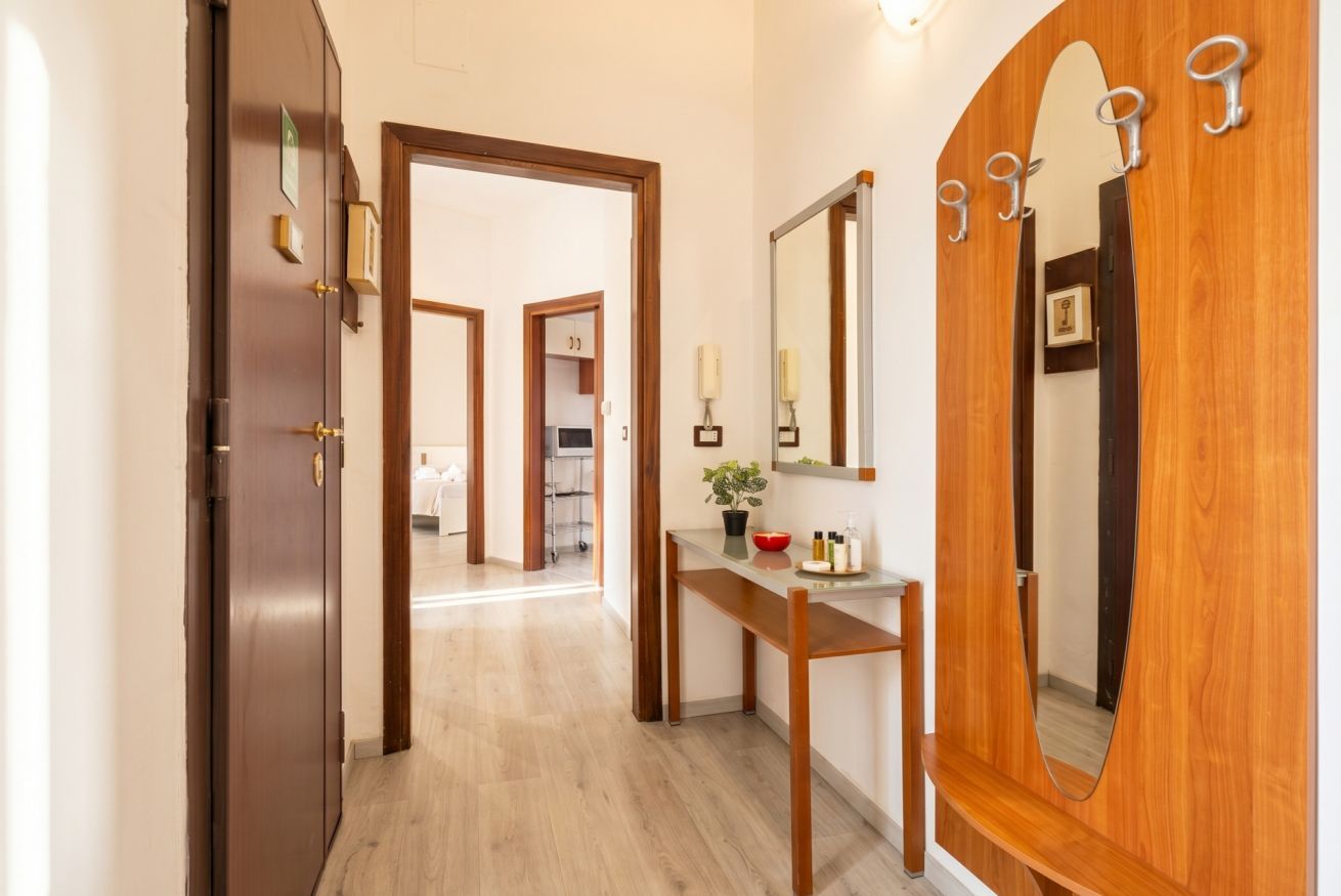 A hallway with a wooden door, a mirror, and a bench with toiletries.