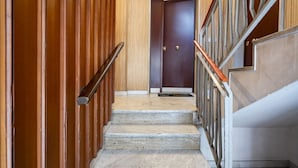 Una scala con rivestimenti in legno su un lato e corrimano in metallo sull'altro, che conduce a un'oscura porta di legno in cima.