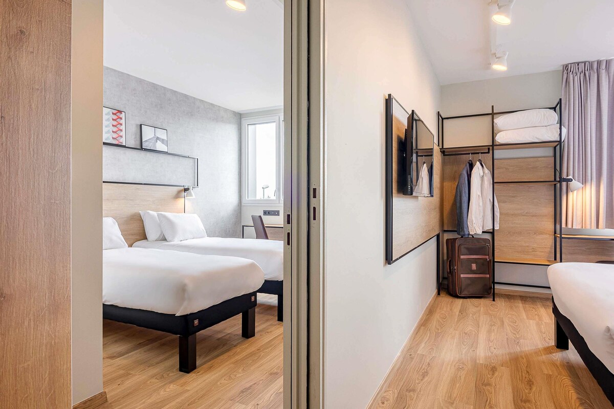 Une chambre d’hôtel avec deux lits, une armoire, un bureau et une fenêtre.