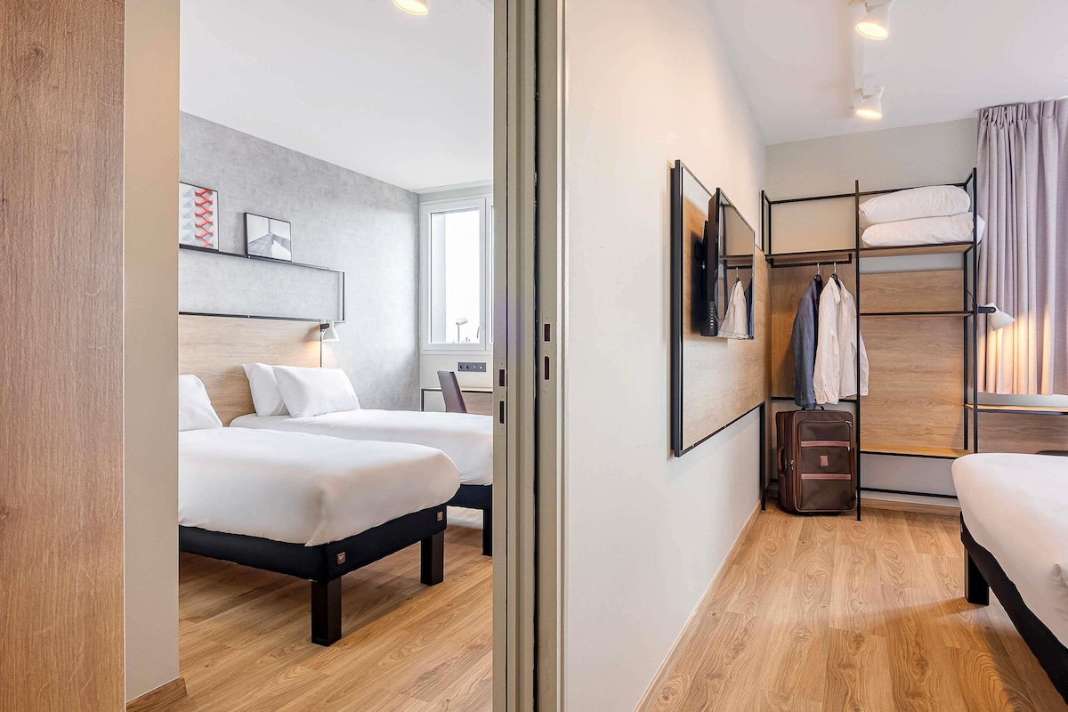 A hotel room with two beds, a wardrobe, a desk, and a window.