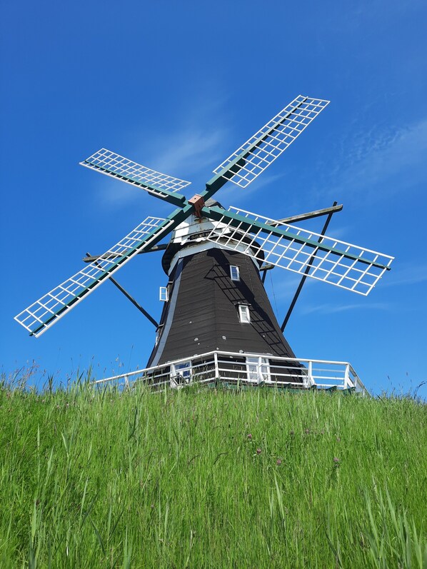 A windmill with four blades, a black tower, and a white railing around the base.