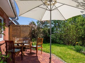 Un patio al aire libre con una mesa, sillas, un paraguas grande y un muro de ladrillo.