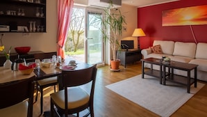 Een woonkamer met een bank, een salontafel, een eettafel met stoelen, een televisie, een potplant en een rode muur.
