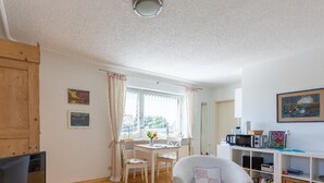 Un salon confortable avec un téléviseur, un fauteuil blanc, une table à manger avec des chaises et une bibliothèque.