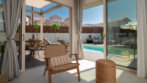A modern room with a large sliding glass door leading to a pool area, wicker furniture, and a view of neighboring buildings. - Alcyone - Gournes NewTown Residences (Heraklion)