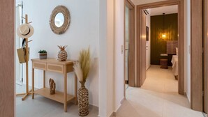A hallway with a wooden console table, a woven vase, a hat on a coat rack, and a mirror on the wall. - Alcyone - Gournes NewTown Residences (Heraklion)
