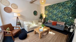 A living room with a sofa, armchair, coffee table, and a wall with a tropical leaf pattern. - The Mews - Worcester City - Gated - Self Check In - WIFI - 2 Doubles - Sleeps 6 (Worcester)