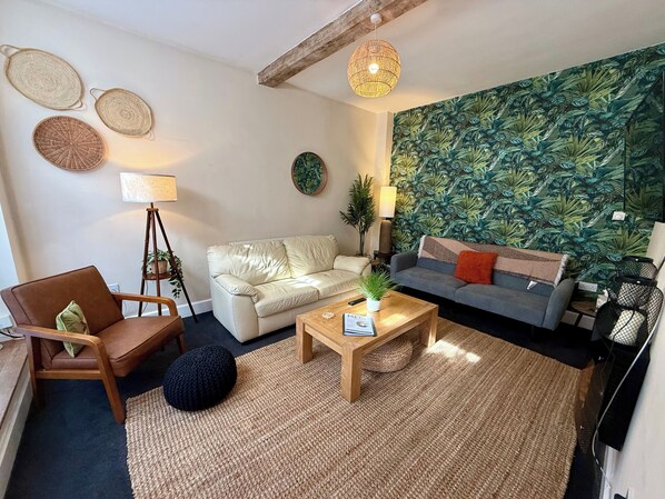 Un salon comprenant un canapé, un fauteuil, une table basse et un mur orné d’un motif de feuilles tropicales.