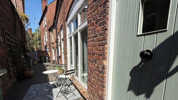 A narrow alleyway with brick buildings, a door with a window, and outdoor furniture. - The Mews - Worcester City - Gated - Self Check In - WIFI - 2 Doubles - Sleeps 6 (Worcester)