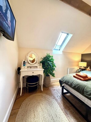 Une chambre à coucher avec un lit, un bureau doté d’un miroir, une plante en pot, un radiateur et un téléviseur fixé au mur.