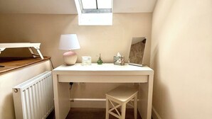 A small, white room with a slanted ceiling, a radiator, a desk with a chair, a small table with a lamp, and a window. - The Mews - Worcester City - Gated - Self Check In - WIFI - 2 Doubles - Sleeps 6 (Worcester)