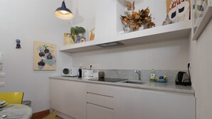 A modern kitchen with white cabinets, a marble countertop, and a yellow chair. - Oltrarno Art House - Florence (Firenze)