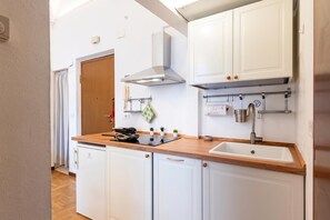 A compact kitchen with white cabinets, a wooden countertop, a built-in stove, and a sink.