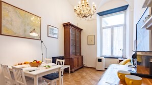 A dining area with a wooden table, white chairs, a chandelier, and a large window with curtains. - Central Apartment Porta Soprana Genova (Genoa)