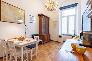 A dining area with a wooden table, white chairs, a chandelier, and a large window with curtains. - Central Apartment Porta Soprana Genova (Genoa)