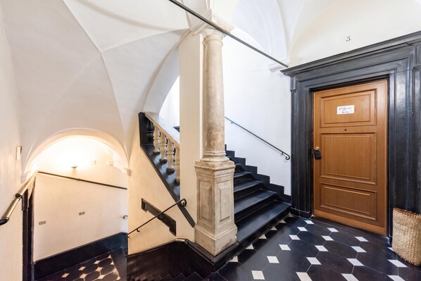 A staircase with a black and white checkered floor, a wooden door with a sign, and a column with a metal handrail.