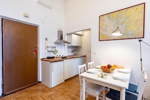 Cocina compacta con armarios blancos, encimera de madera y comedor con una mesa para dos.