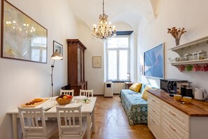 A cozy room with a dining table, chairs, a sofa, a TV, and a kitchen area with cabinets and a microwave.