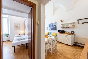 A hotel room with a bed, a small table with a plant, a sofa, a kitchen area with a coffee machine, and a dining table with chairs. - Central Apartment Porta Soprana Genova (Genoa)