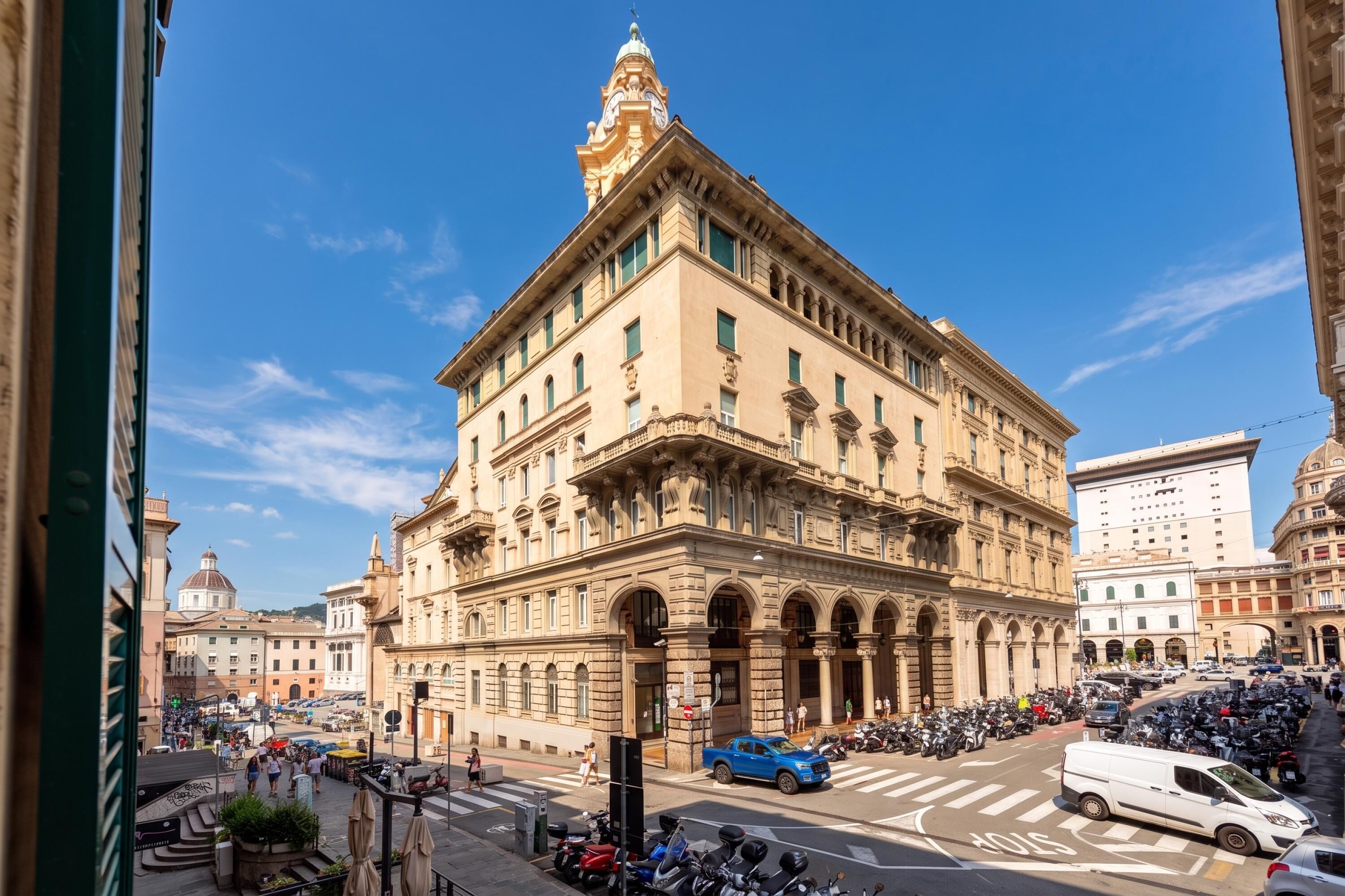 Un edificio histórico con arquitectura clásica, un patio central y una vista a la calle con vehículos estacionados y peatones.