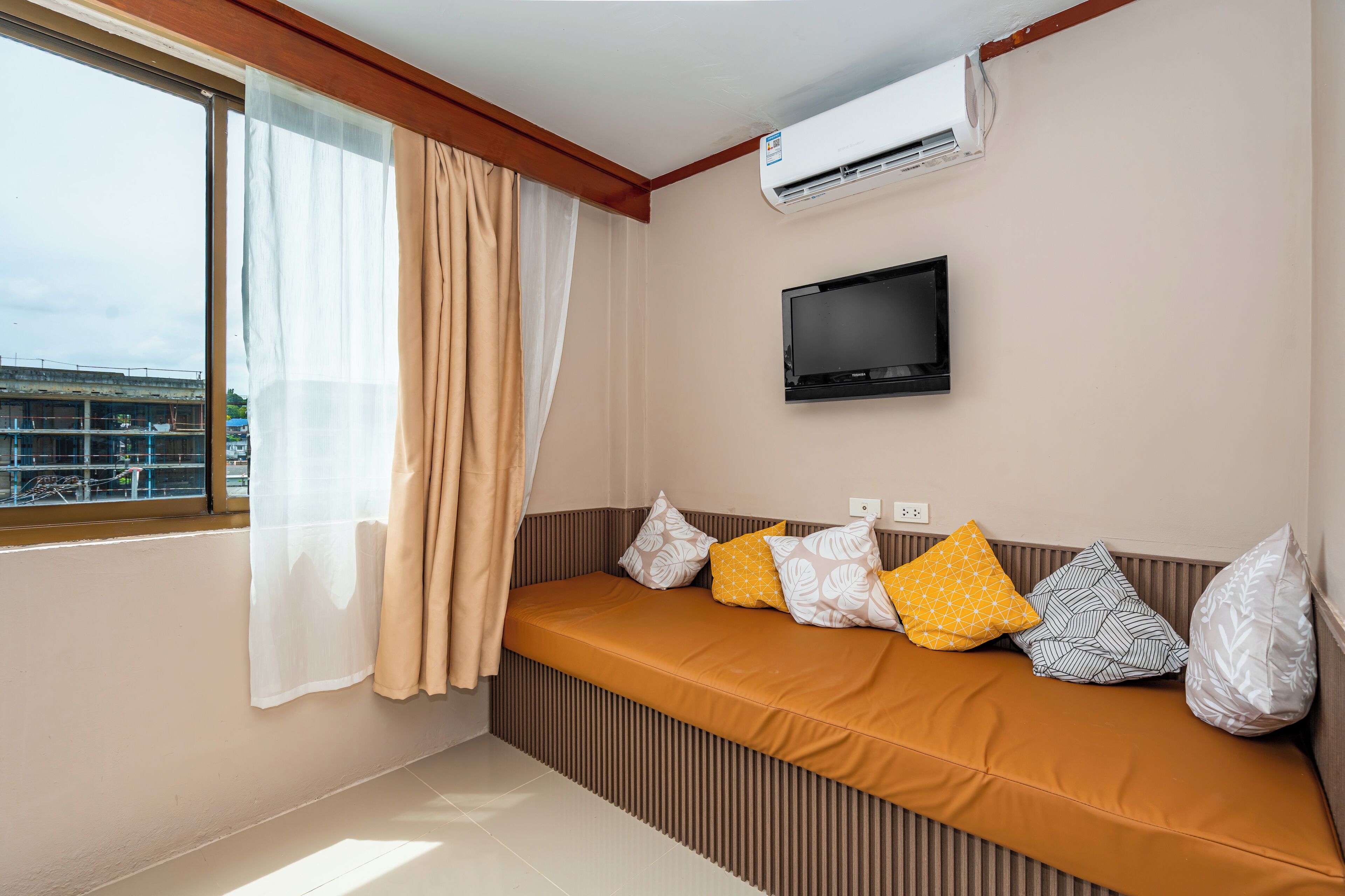A room with a window, air conditioning unit, television, and a sofa with patterned cushions.