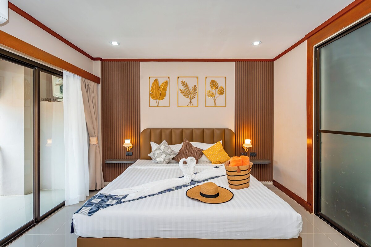A modern hotel room with a large bed, a sliding glass door, and a view of the outdoors.