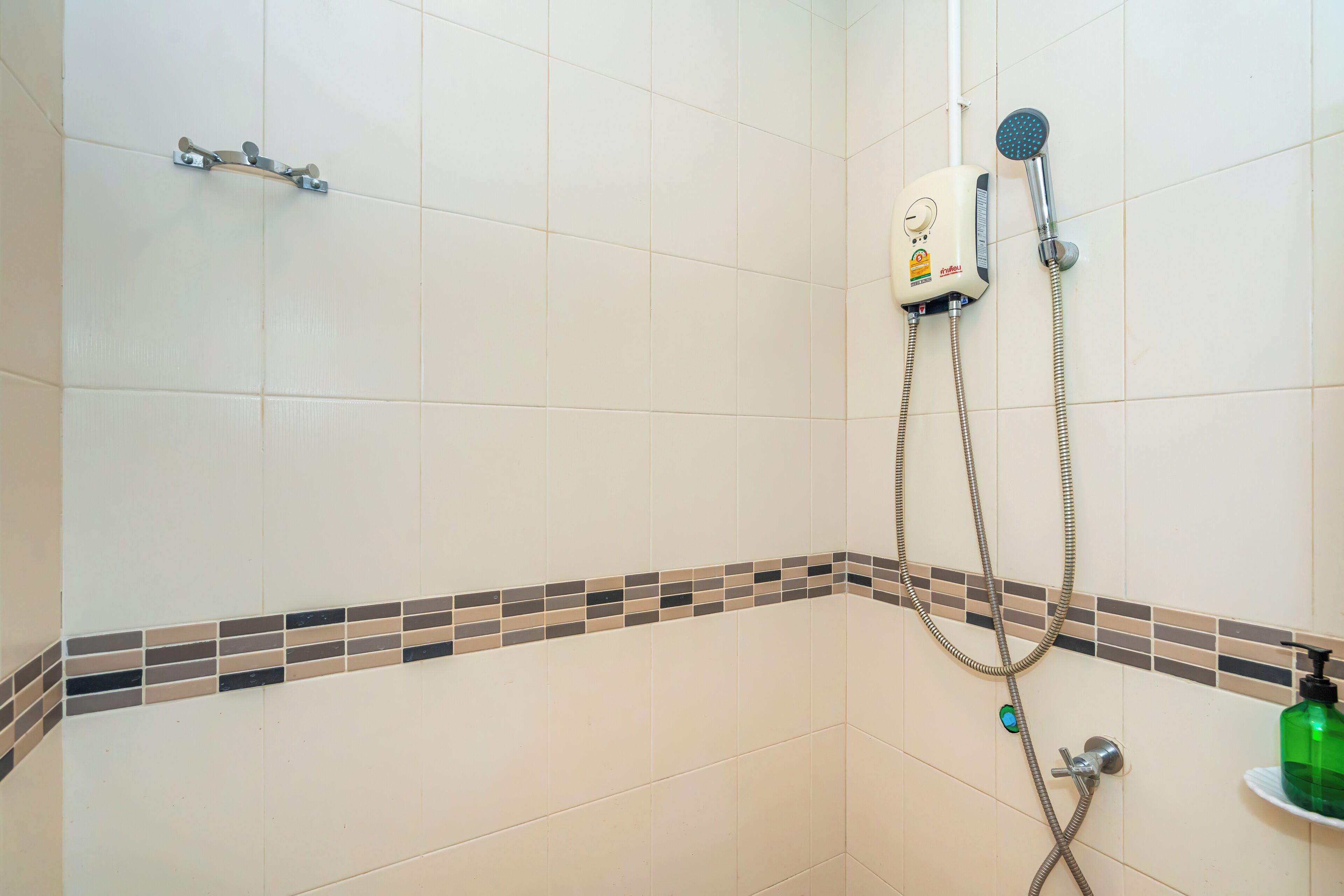 Un espace douche équipé d’un pommeau de douche à main, d’un panneau de commande fixé au mur et d’un sol carrelé agrémenté d’une bordure décorative.