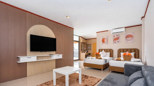A modern hotel room with a flat-screen TV mounted on the wall, a sofa, a bed with two pillows and a striped blanket, and a small white table. - The Outdoor Kata (Karon)