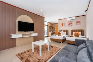 A modern hotel room with a flat-screen TV mounted on the wall, a sofa, a bed with two pillows and a striped blanket, and a small white table. - The Outdoor Kata (Karon)