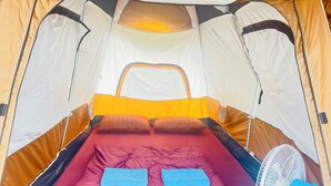 Een tent met een bed, kussens en een ventilator.