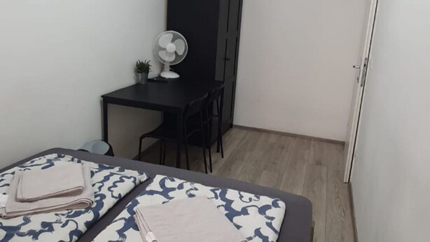 A small room with a bed, a desk, a chair, a fan, and a wardrobe. - Comfortable Room 15 Min to Enkplatz Metro (Vienna)