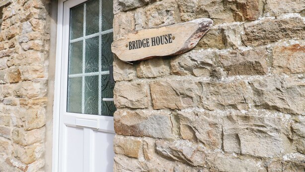 Un muro de piedra con un letrero de madera que dice "Bridge House".