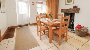 Un comedor con una mesa y sillas de madera, un jarrón con flores, una chimenea y una puerta.