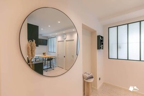A hallway with a round mirror reflecting a dining area, a small table with books, and a wall-mounted cabinet.