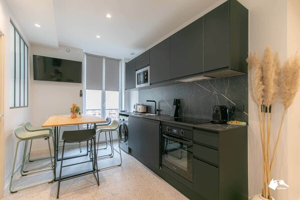 A modern kitchen with dark cabinetry, a central island, and a dining area with chairs.