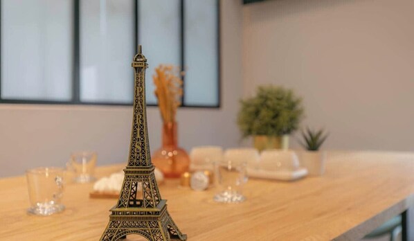 Une maquette de la Tour Eiffel posée sur une table en bois, avec des verres en verre transparent et un vase en arrière-plan.