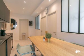 A modern kitchen with a wooden table, a blue chair, and a clock on the wall. - MBA - Raincy 3 - Magnificent Apartment (Villemomble)