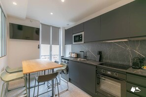 A modern kitchen with a wooden table and chairs, a built-in oven, and a microwave. - MBA - Raincy 3 - Magnificent Apartment (Villemomble)