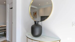 Un intérieur moderne avec un grand miroir rond posé sur une console en marbre, un vase foncé et, au fond, un aperçu d’une cuisine.