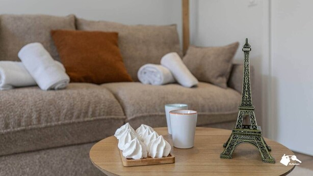 Un salon avec un canapé beige, une petite table en bois sur laquelle est posée une maquette de la Tour Eiffel, une tasse blanche et une assiette de crème fouettée.