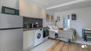 Une chambre d’hôtel compacte comprenant un coin cuisine, un lave-linge, un lit avec vue et une petite table.