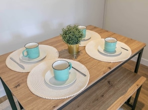 Een houten tafel met vier turquoise kopjes en schoteltjes, elk met een lepel, en een kleine potplant in het midden.
